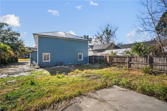 rear view of property featuring metal roof, central AC, and fence