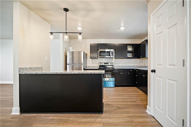 kitchen with light stone counters, light wood-style flooring, appliances with stainless steel finishes, a peninsula, and dark cabinetry