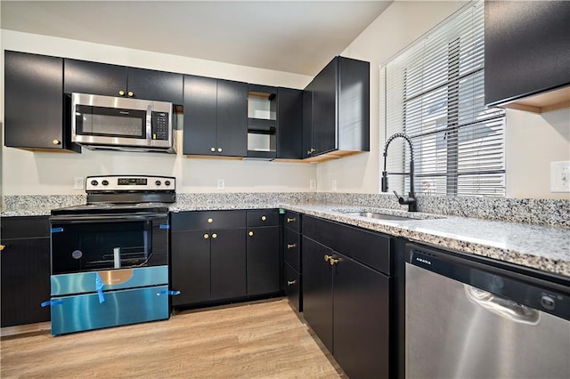 kitchen with light stone counters, light wood-style flooring, a sink, stainless steel appliances, and dark cabinets