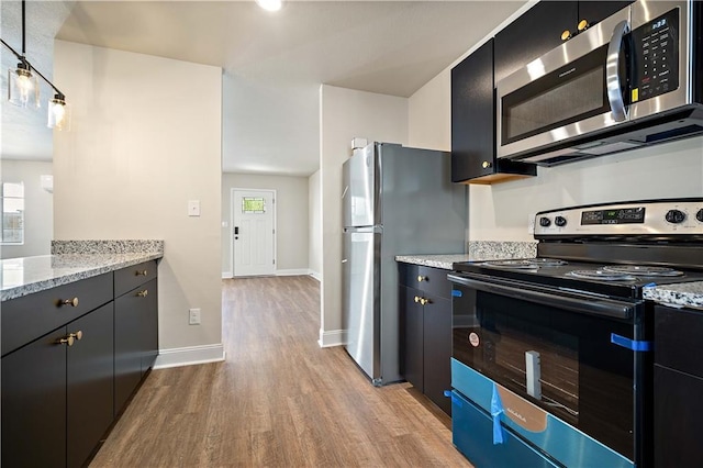 kitchen featuring light wood-type flooring, baseboards, appliances with stainless steel finishes, and dark cabinetry