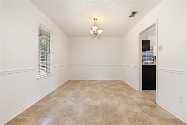 spare room with an inviting chandelier, sink, and a textured ceiling