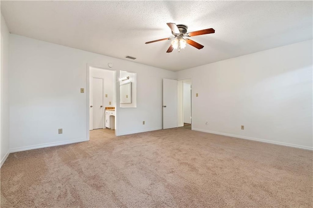 unfurnished bedroom with ceiling fan, light colored carpet, a textured ceiling, and ensuite bath