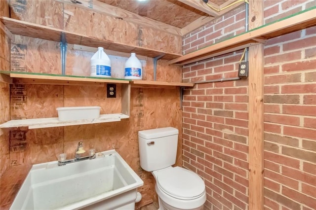 bathroom featuring sink, brick wall, and toilet