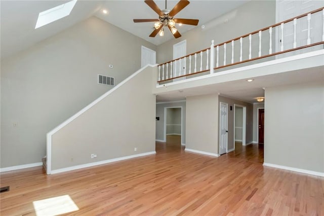 unfurnished living room with high vaulted ceiling, ceiling fan, a skylight, and light wood-type flooring