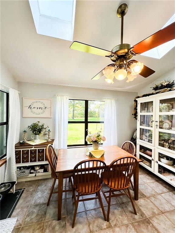 dining area with ceiling fan and lofted ceiling with skylight