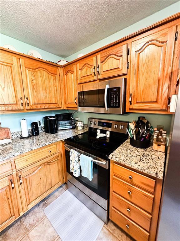 kitchen featuring light stone countertops, a textured ceiling, appliances with stainless steel finishes, and light tile patterned flooring