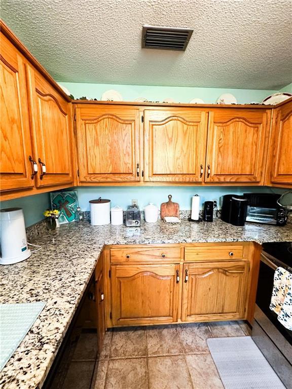 kitchen with light tile patterned floors, light stone counters, stainless steel electric stove, and a textured ceiling