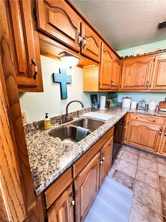 kitchen featuring sink, black dishwasher, light stone countertops, a textured ceiling, and light tile patterned floors