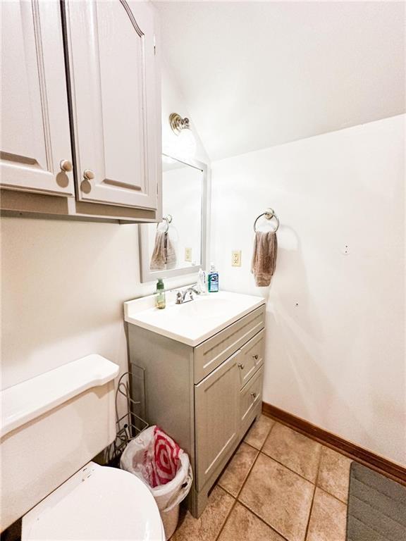 bathroom with tile patterned floors, vanity, lofted ceiling, and toilet