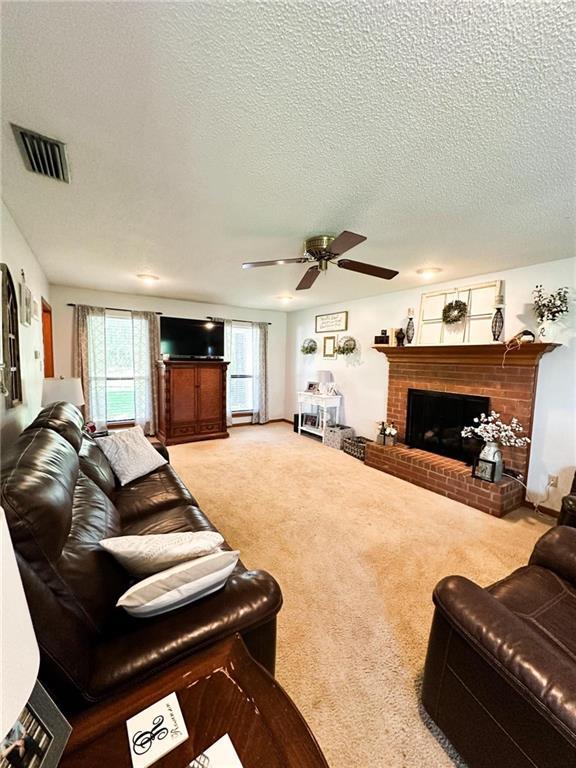 carpeted living room with ceiling fan, a brick fireplace, and a textured ceiling