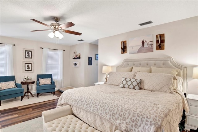 bedroom featuring a ceiling fan, visible vents, dark wood-style flooring, and a textured ceiling