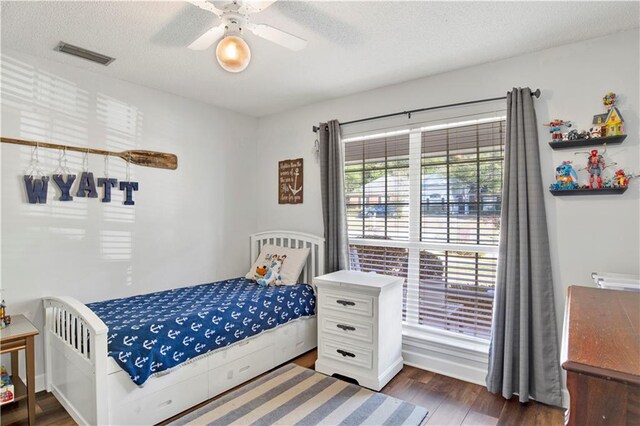 bedroom with visible vents, a textured ceiling, a ceiling fan, and wood finished floors