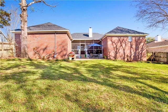 rear view of property with a chimney, fence, a yard, and a sunroom