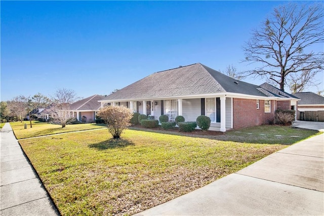 view of front of property featuring brick siding, covered porch, a shingled roof, and a front yard