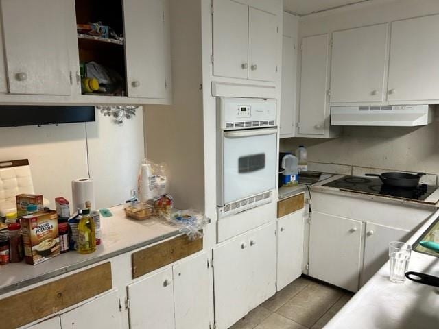 kitchen featuring white oven, black electric cooktop, light tile patterned floors, white cabinets, and extractor fan