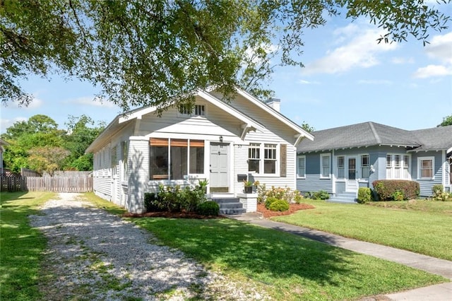 bungalow-style house featuring driveway, a chimney, a front lawn, and fence