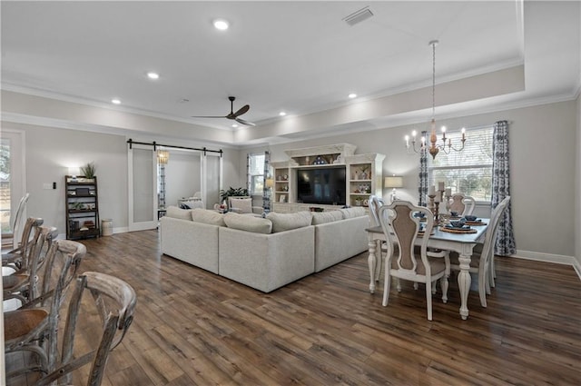 living room featuring ornamental molding, dark hardwood / wood-style floors, a tray ceiling, a barn door, and ceiling fan with notable chandelier