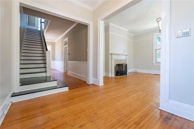1703 Dauphin St, Mobile, AL 36604 - unfurnished living room featuring ornamental molding, wood finished floors, stairs, a wainscoted wall, and a fireplace with flush hearth