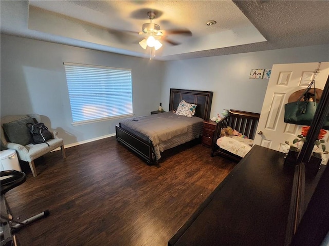 bedroom featuring ceiling fan, dark hardwood / wood-style floors, a textured ceiling, and a tray ceiling