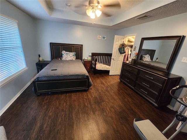 bedroom with a raised ceiling, dark wood-type flooring, ceiling fan, and a spacious closet