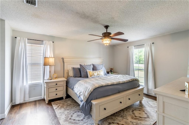 bedroom with a ceiling fan, a textured ceiling, visible vents, wood finished floors, and baseboards