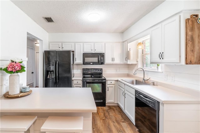 kitchen with a sink, a textured ceiling, white cabinetry, visible vents, and black appliances
