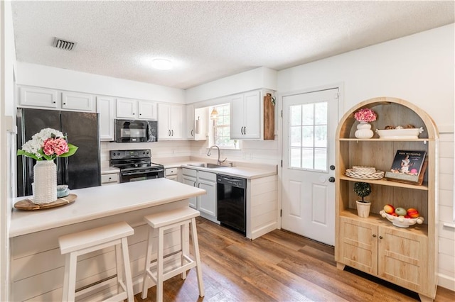 kitchen with a sink, a textured ceiling, wood finished floors, visible vents, and black appliances