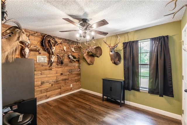 empty room featuring wood finished floors, baseboards, ceiling fan, wooden walls, and a textured ceiling