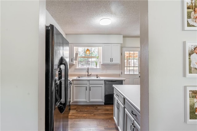 kitchen featuring a textured ceiling, dark wood finished floors, a sink, light countertops, and black appliances