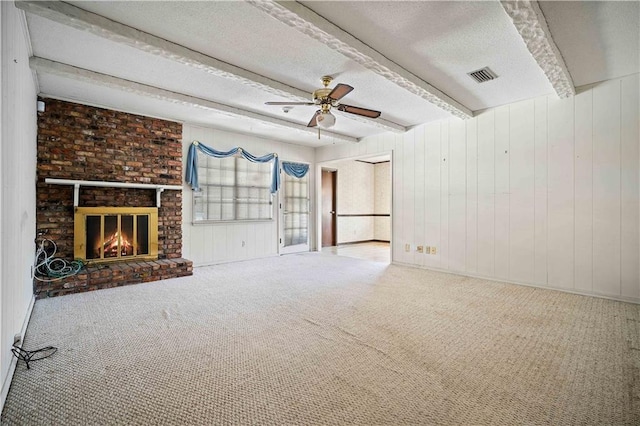 unfurnished living room with a textured ceiling, a brick fireplace, ceiling fan, beam ceiling, and carpet