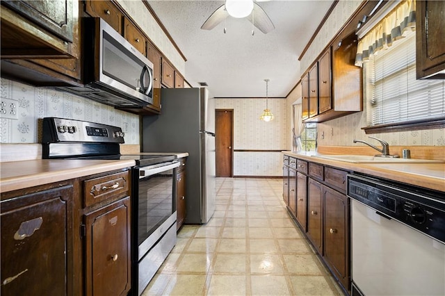 kitchen featuring appliances with stainless steel finishes, a textured ceiling, sink, crown molding, and decorative light fixtures