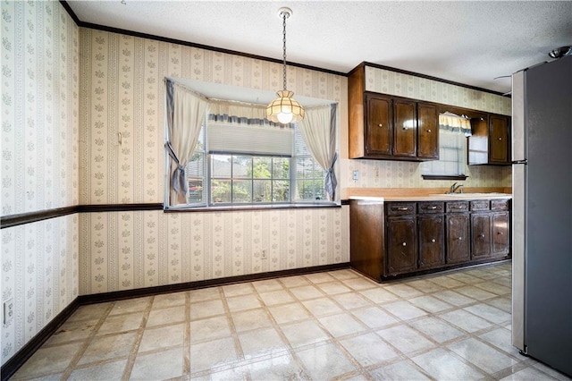 kitchen featuring a textured ceiling, stainless steel appliances, dark brown cabinetry, pendant lighting, and ornamental molding