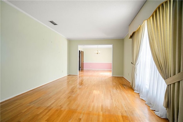 spare room with plenty of natural light, a notable chandelier, ornamental molding, and light wood-type flooring