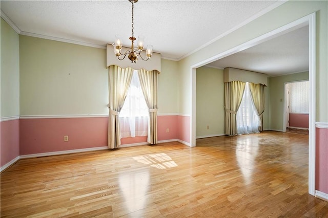 unfurnished room featuring light hardwood / wood-style flooring, a textured ceiling, a notable chandelier, and crown molding