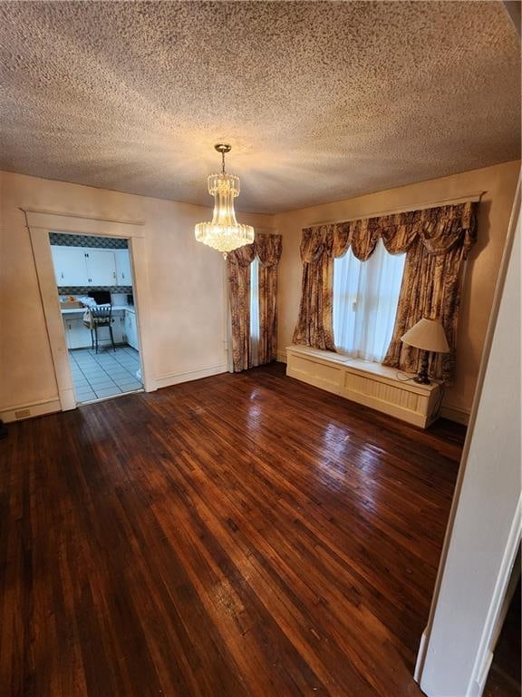 unfurnished room with a notable chandelier, a textured ceiling, and wood-type flooring