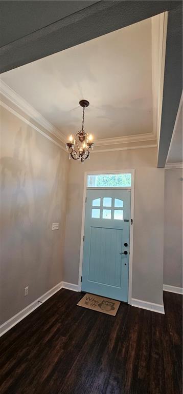 entrance foyer featuring dark hardwood / wood-style flooring, an inviting chandelier, and ornamental molding