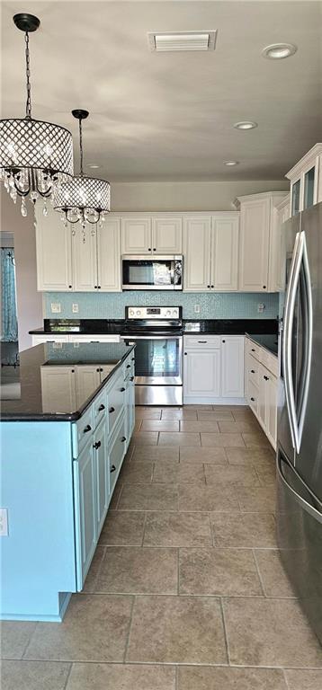 kitchen with appliances with stainless steel finishes, pendant lighting, backsplash, and white cabinets