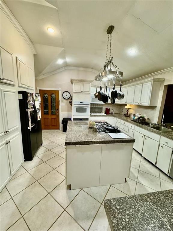 kitchen with black fridge, stainless steel gas cooktop, white cabinets, a kitchen island, and lofted ceiling