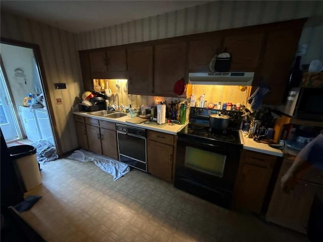kitchen with black appliances, a sink, under cabinet range hood, wallpapered walls, and light countertops
