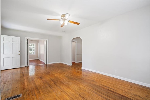 unfurnished room with arched walkways, visible vents, hardwood / wood-style floors, and baseboards