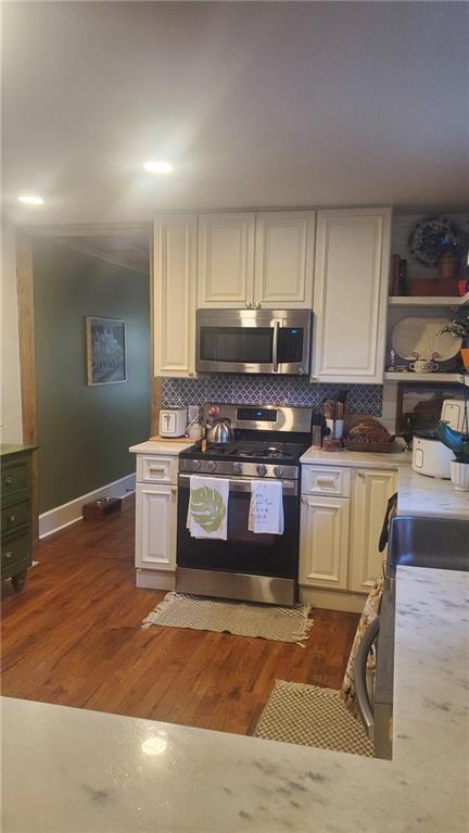 kitchen with white cabinets, dark hardwood / wood-style flooring, appliances with stainless steel finishes, and tasteful backsplash