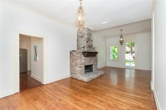 unfurnished living room featuring a notable chandelier, a brick fireplace, light hardwood / wood-style flooring, crown molding, and brick wall