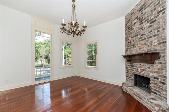 unfurnished living room featuring an inviting chandelier, a brick fireplace, dark hardwood / wood-style floors, and brick wall