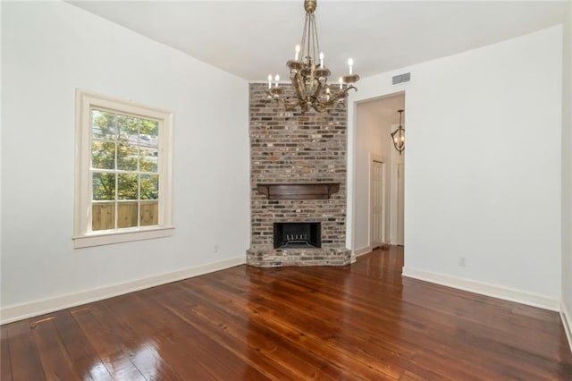 unfurnished living room featuring dark hardwood / wood-style floors, brick wall, a notable chandelier, and a brick fireplace