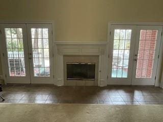 unfurnished living room with tile patterned floors, french doors, a healthy amount of sunlight, and a glass covered fireplace