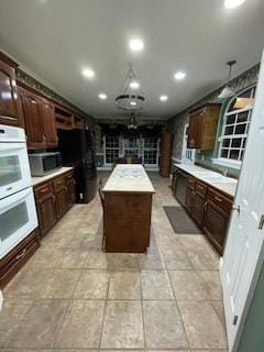 kitchen with dark brown cabinets, a kitchen island, double oven, light countertops, and freestanding refrigerator