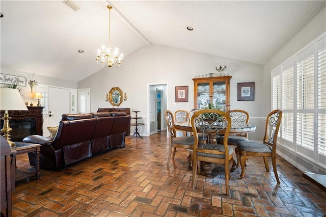 dining area with visible vents, high vaulted ceiling, an inviting chandelier, brick floor, and a glass covered fireplace