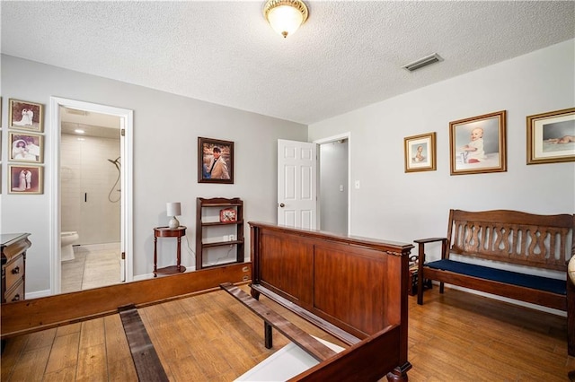 bedroom with hardwood / wood-style floors, baseboards, visible vents, and a textured ceiling