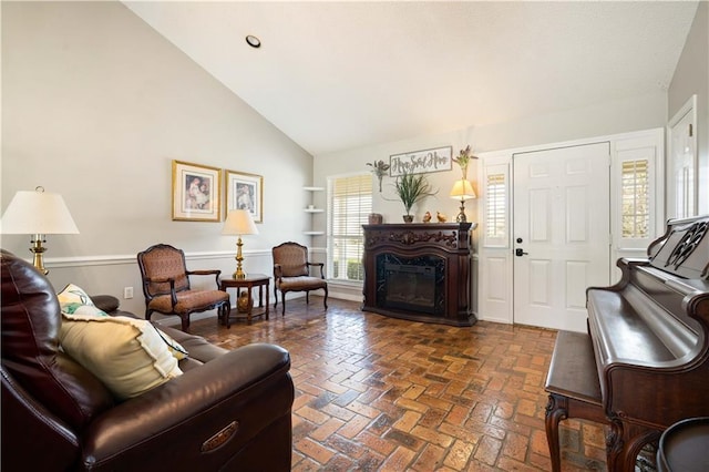 living room featuring brick floor, high vaulted ceiling, and a glass covered fireplace