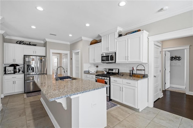 kitchen featuring decorative backsplash, light stone countertops, a kitchen island with sink, stainless steel appliances, and a sink